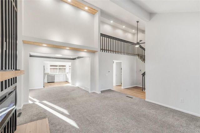 unfurnished living room featuring ceiling fan, light colored carpet, and a high ceiling