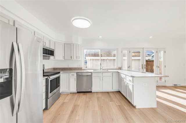 kitchen featuring appliances with stainless steel finishes, a wealth of natural light, light wood-type flooring, and white cabinets