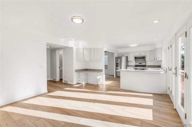 kitchen with sink, white cabinetry, light wood-type flooring, kitchen peninsula, and stainless steel appliances