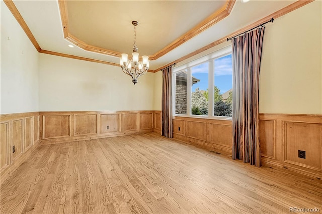 unfurnished room with a raised ceiling, a chandelier, light wood-type flooring, and ornamental molding