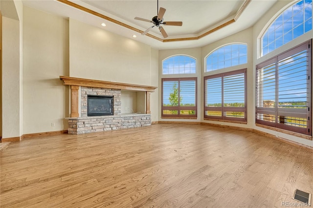 unfurnished living room with a tray ceiling, ceiling fan, a fireplace, and light hardwood / wood-style floors