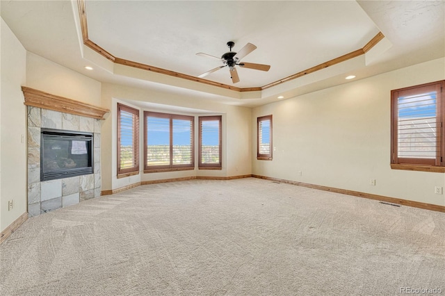 unfurnished living room featuring ornamental molding, a raised ceiling, ceiling fan, carpet floors, and a tiled fireplace