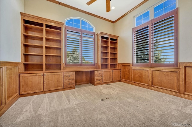 unfurnished office with crown molding, ceiling fan, built in desk, a wealth of natural light, and light colored carpet