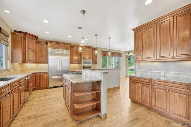 kitchen with a center island, stainless steel appliances, light stone counters, a chandelier, and decorative light fixtures