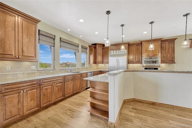 kitchen with light stone countertops, sink, hanging light fixtures, appliances with stainless steel finishes, and light wood-type flooring