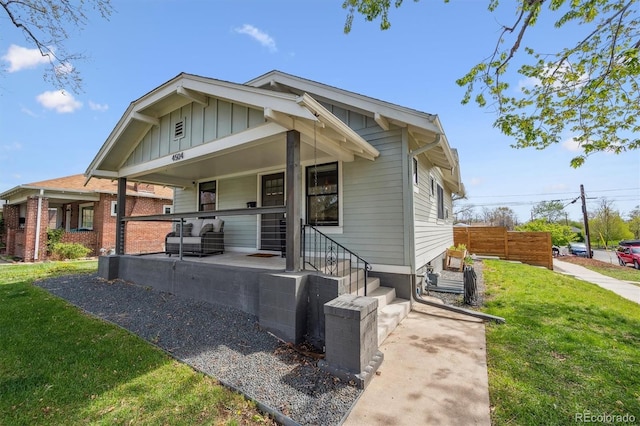 bungalow-style home with board and batten siding, fence, covered porch, and a front yard