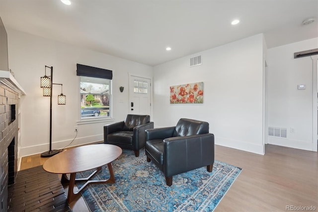 living room with a brick fireplace, wood finished floors, and visible vents