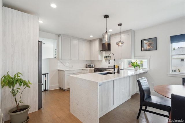 kitchen featuring light countertops, wall chimney exhaust hood, a peninsula, light wood-type flooring, and backsplash
