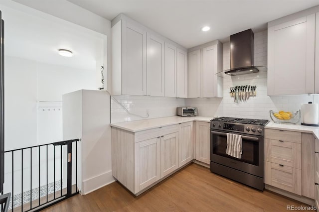 kitchen featuring light wood-style floors, light countertops, wall chimney exhaust hood, stainless steel range with gas cooktop, and decorative backsplash
