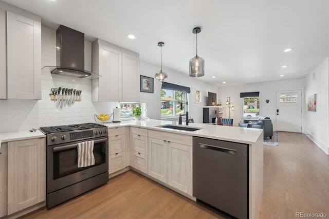 kitchen featuring appliances with stainless steel finishes, light wood-style flooring, a peninsula, and wall chimney exhaust hood