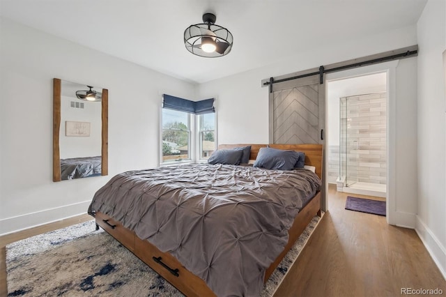 bedroom featuring visible vents, wood finished floors, baseboards, a barn door, and connected bathroom