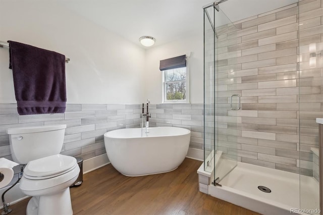 full bathroom with tile walls, a shower stall, wood finished floors, toilet, and a soaking tub