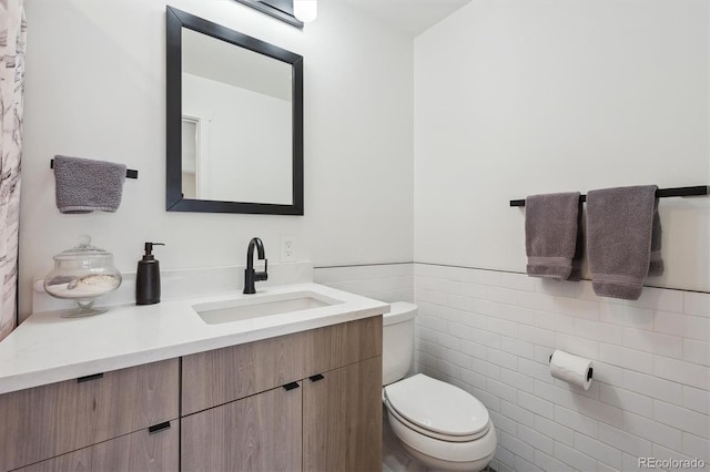 bathroom with toilet, tile walls, a wainscoted wall, and vanity