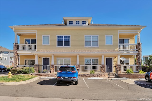 view of front facade featuring covered porch, uncovered parking, and a balcony