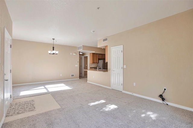 unfurnished living room featuring a chandelier, light colored carpet, a sink, and baseboards