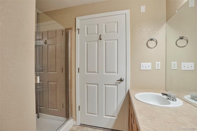 full bath featuring a textured wall, a shower stall, and vanity