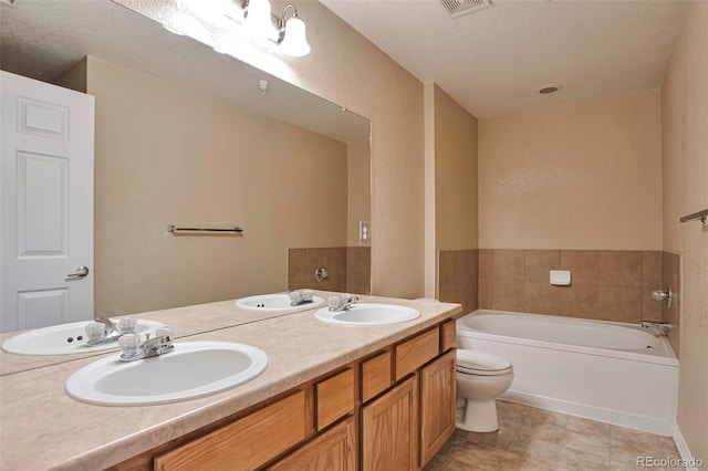 bathroom featuring a bath, a textured ceiling, double vanity, and toilet