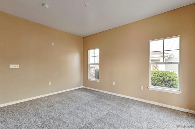 carpeted empty room featuring baseboards and a smoke detector