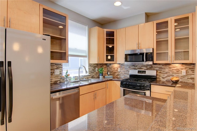 kitchen featuring light brown cabinets, appliances with stainless steel finishes, dark stone counters, and a sink