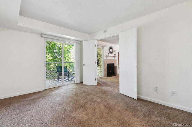 unfurnished room with a tiled fireplace, a textured ceiling, and carpet