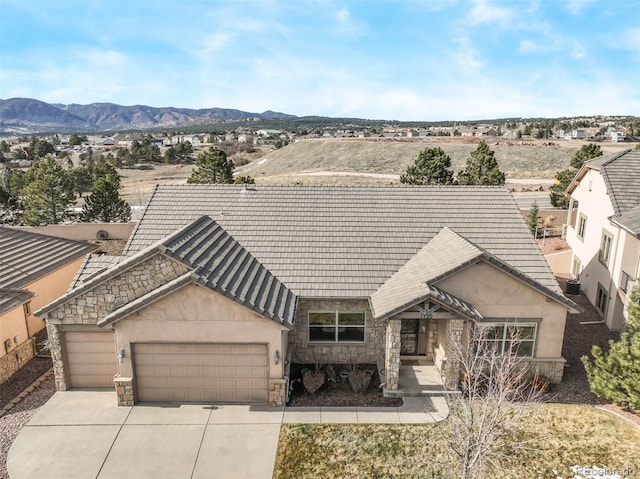 view of front facade featuring stucco siding, stone siding, a mountain view, concrete driveway, and a garage