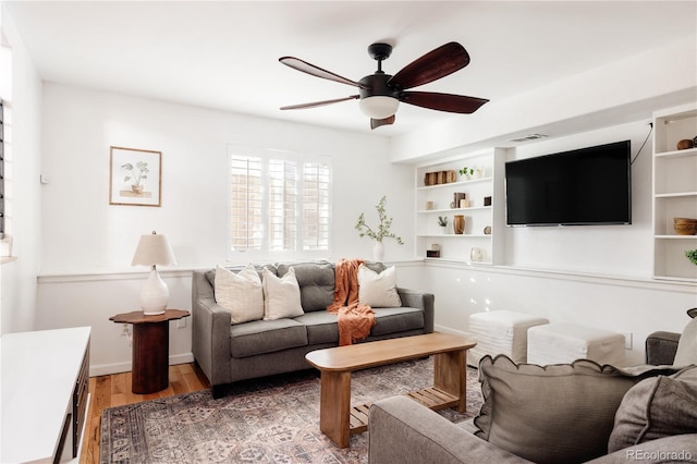 living room with hardwood / wood-style floors, built in shelves, and ceiling fan