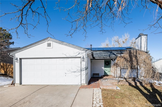 single story home featuring a garage, concrete driveway, and roof mounted solar panels