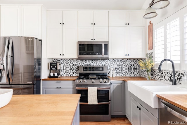 kitchen featuring tasteful backsplash, appliances with stainless steel finishes, white cabinetry, a sink, and butcher block countertops