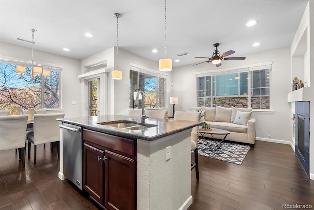 kitchen with dark hardwood / wood-style flooring, a kitchen island with sink, sink, and hanging light fixtures