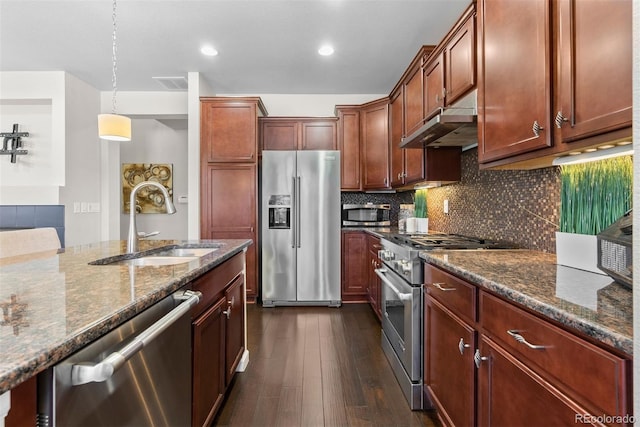 kitchen with sink, decorative light fixtures, premium appliances, dark stone counters, and decorative backsplash