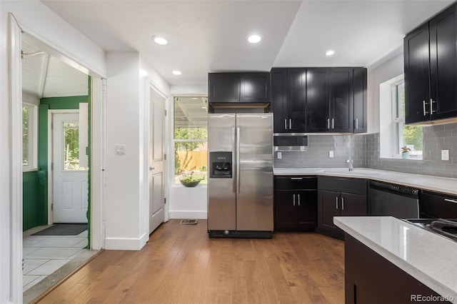 kitchen with tasteful backsplash, sink, light hardwood / wood-style floors, stainless steel appliances, and light stone countertops