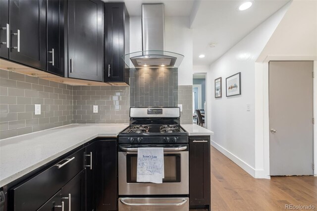 kitchen with stainless steel gas stove, light stone counters, light hardwood / wood-style floors, decorative backsplash, and exhaust hood