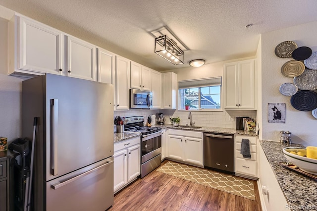 5757 S Algonquian Way Unit E, Aurora, CO 80016 - kitchen featuring appliances with stainless steel finishes, light wood-style floors, white cabinetry, backsplash, and a textured ceiling