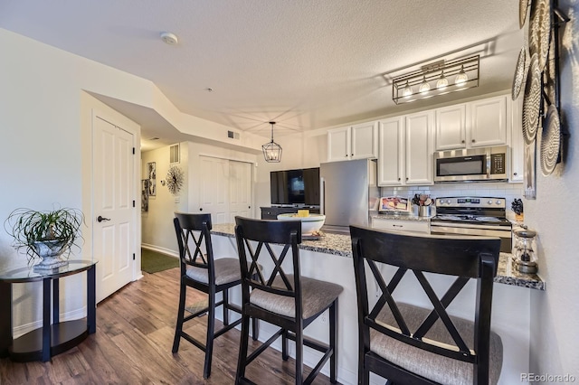 5757 S Algonquian Way Unit E, Aurora, CO 80016 - kitchen with stainless steel appliances, dark wood finished floors, white cabinets, a breakfast bar, and a peninsula