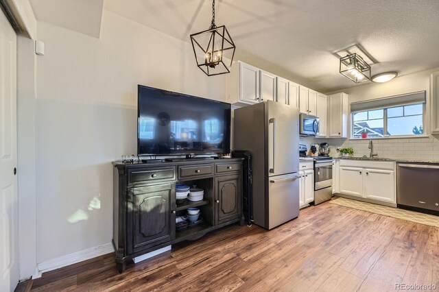 5757 S Algonquian Way Unit E, Aurora, CO 80016 - kitchen featuring stainless steel appliances, white cabinets, light wood finished floors, tasteful backsplash, and a chandelier