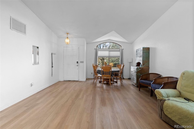 dining space featuring light wood finished floors, baseboards, visible vents, and vaulted ceiling