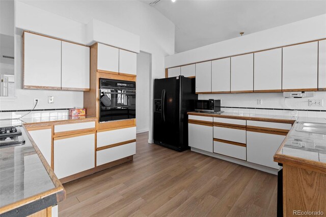 kitchen with black appliances, light wood-style flooring, high vaulted ceiling, and white cabinets