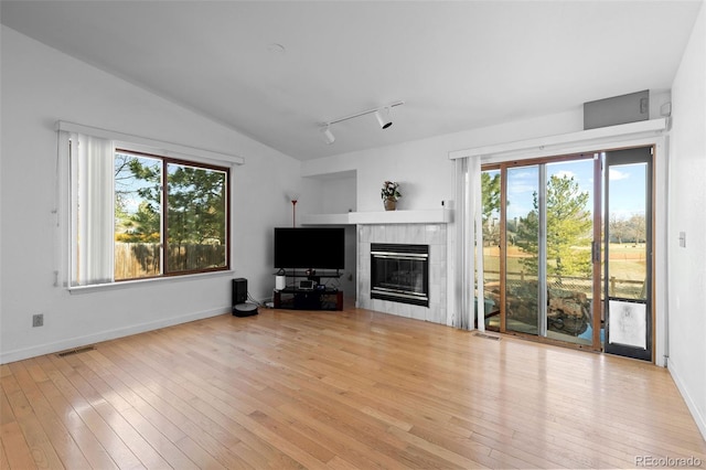 unfurnished living room with a tile fireplace, wood-type flooring, visible vents, and vaulted ceiling