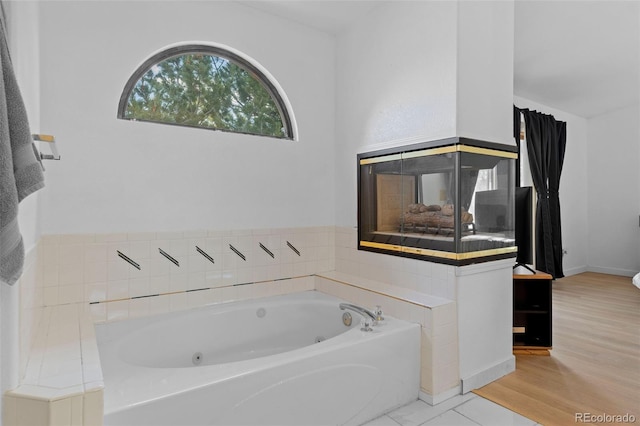 bathroom with a tub with jets, wood finished floors, and baseboards