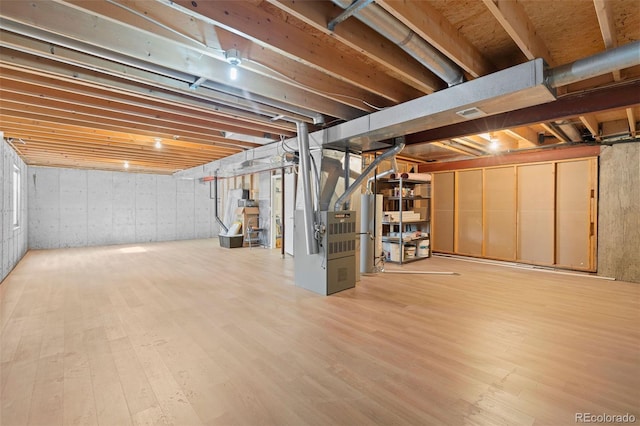 unfinished basement featuring water heater, wood finished floors, and heating unit