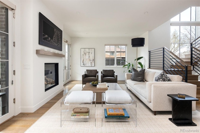 living room with baseboards, a glass covered fireplace, stairway, and wood finished floors