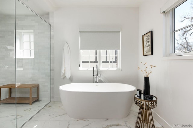 full bathroom featuring marble finish floor, a freestanding bath, tiled shower, and a healthy amount of sunlight