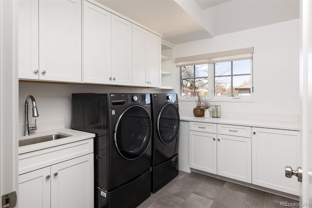 clothes washing area with a sink, cabinet space, and separate washer and dryer