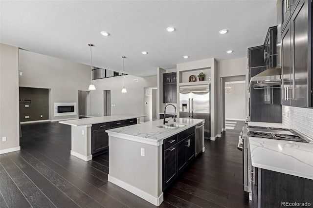 kitchen featuring sink, appliances with stainless steel finishes, light stone countertops, an island with sink, and decorative light fixtures