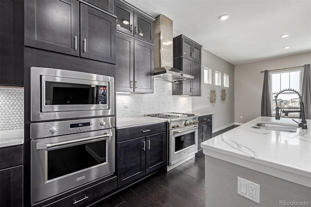 kitchen with wall chimney range hood, sink, appliances with stainless steel finishes, light stone counters, and tasteful backsplash