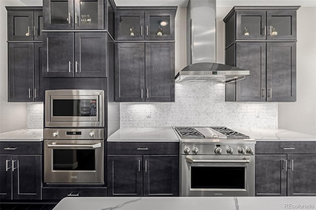 kitchen with stainless steel appliances, light stone countertops, wall chimney range hood, and decorative backsplash