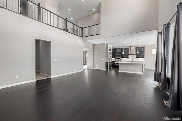 unfurnished living room featuring a towering ceiling, dark hardwood / wood-style flooring, and sink