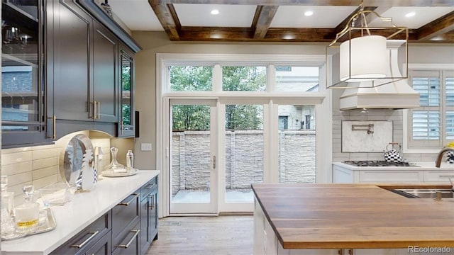 kitchen with coffered ceiling, butcher block counters, custom exhaust hood, beam ceiling, and backsplash