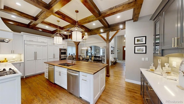 kitchen with appliances with stainless steel finishes, white cabinetry, a kitchen island with sink, butcher block counters, and decorative light fixtures