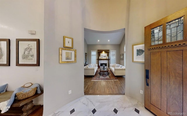 foyer entrance featuring marble finish floor, a fireplace, a towering ceiling, and baseboards